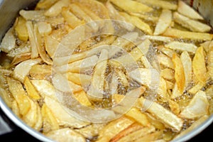 Close-up of French fries potatoes frying in boiling hot oil in a deep fryer at home. French fries, Junk food concept, home made