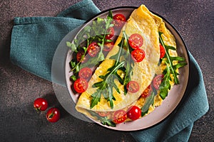 Close up of french omelette filled with cherry tomatoes and arugula on a plate on the table top view