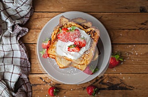 Close-up of french toast with fresh strawberries, coconut shreds and honey, on wooden background, top view