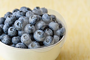 Close up of fresh blueberries in a white ceramic bowl on a yellow crackle background