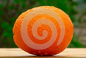 Close up of a fresh bright tasty orange on a wooden table in the garden, natural vegan food