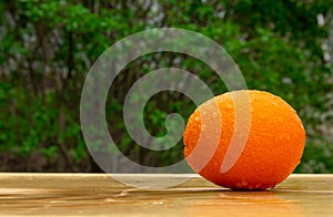 Close up of a fresh bright tasty orange on a wooden table in the garden, natural vegan food