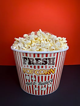 Close up fresh buttery popcorn in a stripped red and white bowl on red background