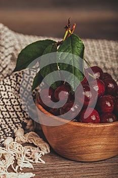 Close up of fresh cherries with green leaves in wooden bowl