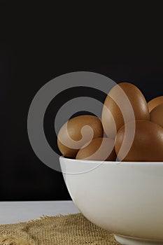 Close up fresh chicken eggs in white bolw on linen tablecloth and white table with copy space