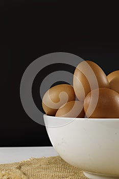 Close up fresh chicken eggs in white bolw on linen tablecloth and white table with copy space