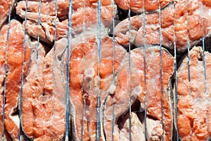 Close-up of fresh coho salmon steaks as a background on a barbecue metal grill - appetizing pieces of fish on an open red fire