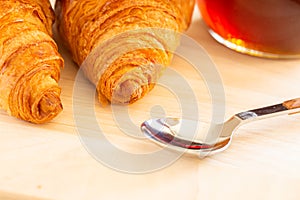 Close up of Fresh croissants, spoon and honey jar over wooden board, breakfast, selective focus