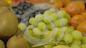 Close-up of fresh delicious green grapes, kiwi fruits and tangerines in grocery store. Tasty healthful food lying on the