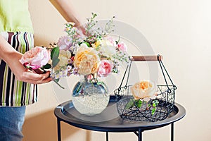 Close up of fresh english roses. Woman makes bouquet in transparent vase of orange yellow pink flowers on table at home