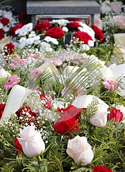 Close up of fresh floral wreaths made of pink and red roses on the grave after a funeral