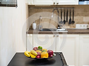 Close-up of fresh fruits on plate. Blurred kicthen in background. Sink, black spoons on wall.