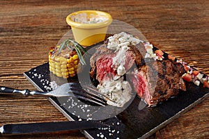Close-up of fresh grilled beef steak with cream mushroom sauce on black board on wooden background