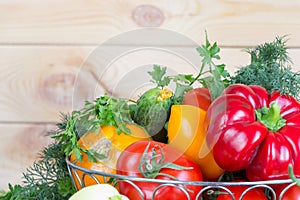 Close up fresh harvested vegetables in wicker basket on wooden table with copy space.