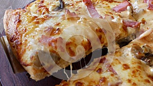Close up of fresh hot mushroom-ham-cheese pizza slices with melting cheese being scooped / taken out of a wooden tray
