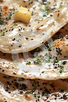 Close-up of fresh, hot tandoori roti or butter naan garnished with black till and green fresh coriander leaves.