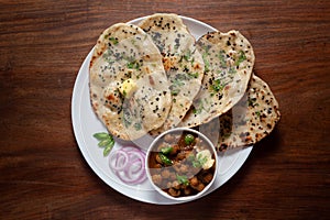 Close-up of fresh, hot tandoori roti or butter naan garnished with black till and green fresh coriander leaves and chole.