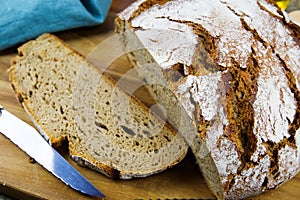 Close up of fresh made german stoneoven bread, cut slice and brown white loaf with crunchy crust on wooden cutting board