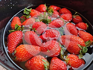 a Close-up of fresh red strawberries lying in a bowl full of water to clean