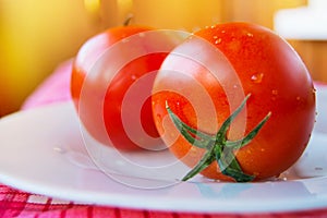 Close-up of fresh ripe tomatoes with water drops and a green peduncle on a white plate, selective focus