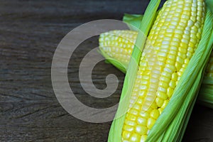 Close up fresh sweet corn cobs with leaves on wood table background