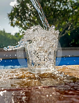 Close-up of fresh water poured into a glass on the edge of the poo