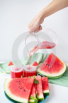 Close-up of fresh watermelon juice or smoothie in glasses with watermelon slices on a white table. A refreshing summer drink is