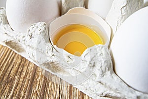 Close-up of fresh white organic chicken eggs in the paper tray and egg yolk on wooden background