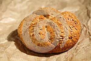 Close up of a fresh, whole wheat small roll bread with sesame seeds on a brown unbleached baking paper