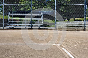 Close up of freshly chalked baseline leading to home plate, with backstop and bleachers, empty baseball field on a sunny day