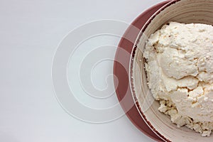 Close-up of freshly made white soft cottage cheese in bowl on white table background. Homemade ricotta cheese.