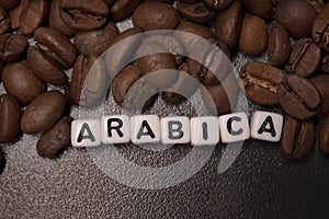 Close up of Freshly roasted coffee beans near word ARABICA written with little white cubes. top view
