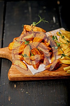 Close-up fried potato wedges on a wooden cutting board. Big portion of baked potatoes with sauce and herbs. Homemade french fries