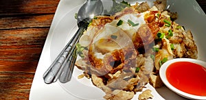 Close up fried rice noodle with chicken, fried egg on top and chili sauce in small bowl on white dish or plate at Thai street food