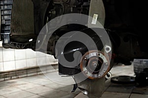 A close-up on front brake system of a car with hub on a lift in a vehicle repair workshop. Auto service industry