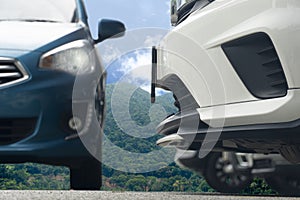 Close-up front bumper white car parking with blurred other cars on asphalt road.