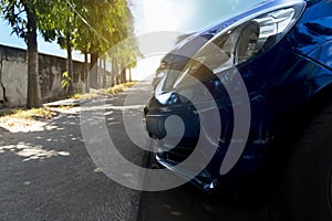 Close up front of dark blue color car. Parking beside of footpath concreate with blurre of other cars.