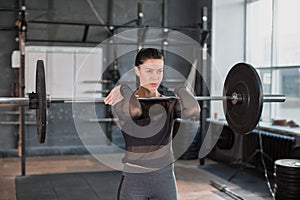 Close up front portriat of a woman is lifting weight while working out with barbell in gym.