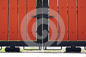 Close up a front veiw of a red wooden slats Sliding gate with a black metal handle in the from of a fence