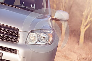 Close up front vew silver SUV car in the forest. Detail of a modern car. Head light