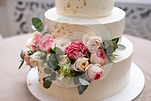 Close up front view of beautiful modern white wedding cake decorated with fresh pink roses with copy space.