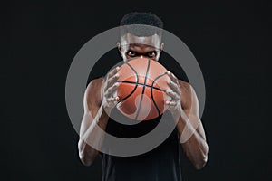 Close up front view shot of afro american male basketball player holding a ball in front of him over black background