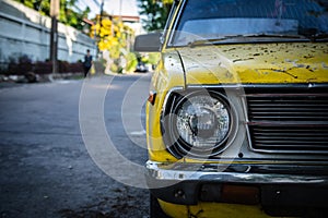 Close up and front view shot with copy space of chrome grill and front light of yellow retro car in grunge condition with rust and