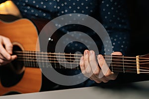 Close-up front view of unrecognizable guitarist male playing acoustic guitar sitting at desk in dark living room