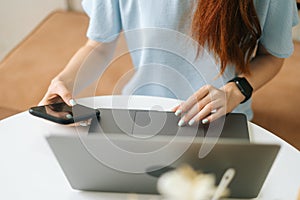Close-up front view of unrecognizable young woman in smart watch using laptop and phone sitting at table in cafe with