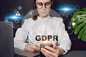 Close up front view young woman holding smartphone, with text GDPR. Data Protection Regulation, sitting at desk near pc. photo