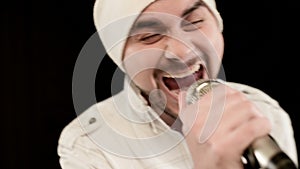 Close-up frontman vocalist rock pop with a stylish beard in white clothes and a hat with a microphone in his hands