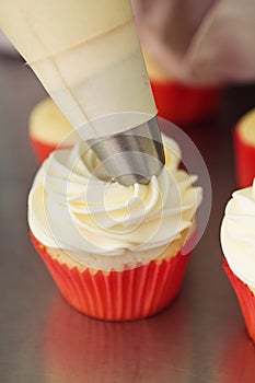 Close up frosting being applied to a vanilla cupcake