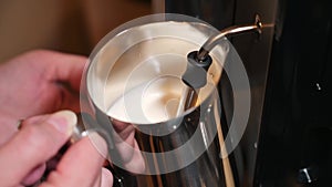 Close-up frothing milk for a cappuccino in an iron pitcher. Preparing latte