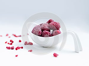 Close up of frozen rasberries in a white bowl on a white background with selective focus.
